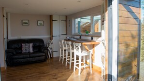 A modern kitchen with white cabinets, a wooden countertop, and a window overlooking a wooden deck. - Mulino Pods (Ashbourne)