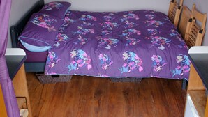 A compact bedroom with a bed, a window with curtains, a wooden floor, and a small wooden chair. - Mulino Pods (Ashbourne)