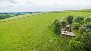 A rural landscape with a wooden house surrounded by greenery and a fenced field. - Mulino Pods (Ashbourne)