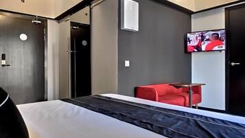 A modern hotel room with a bed, a red sofa, a TV, and a wall-mounted air conditioner.