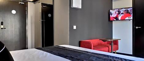 A modern hotel room with a bed, a red sofa, a TV, and a wall-mounted air conditioner.