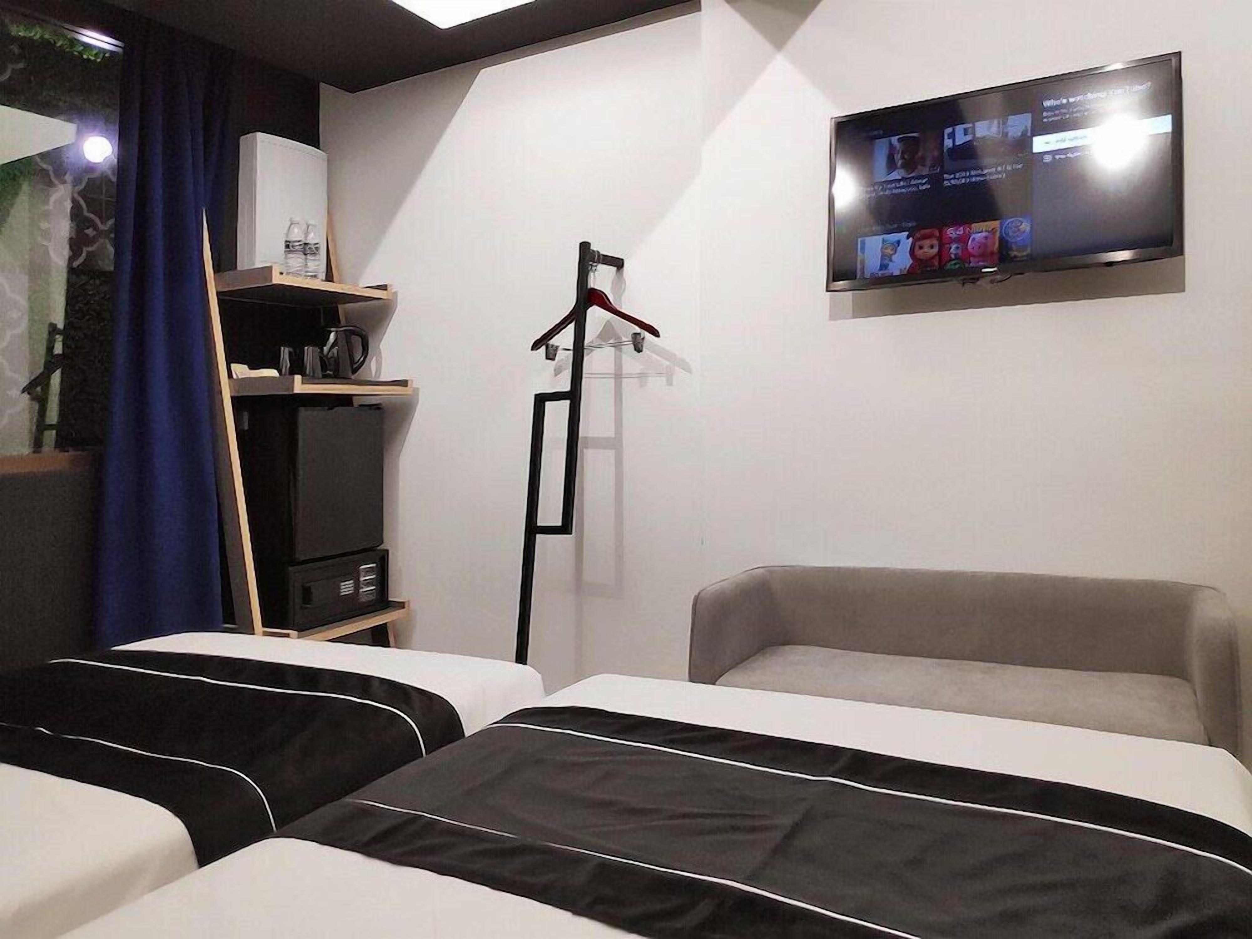 Une chambre d’hôtel avec deux lits, un téléviseur fixé au mur, une armoire et un bureau avec une lampe.