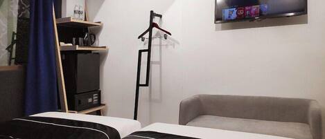 Une chambre d’hôtel avec deux lits, un téléviseur fixé au mur, une armoire et un bureau avec une lampe.