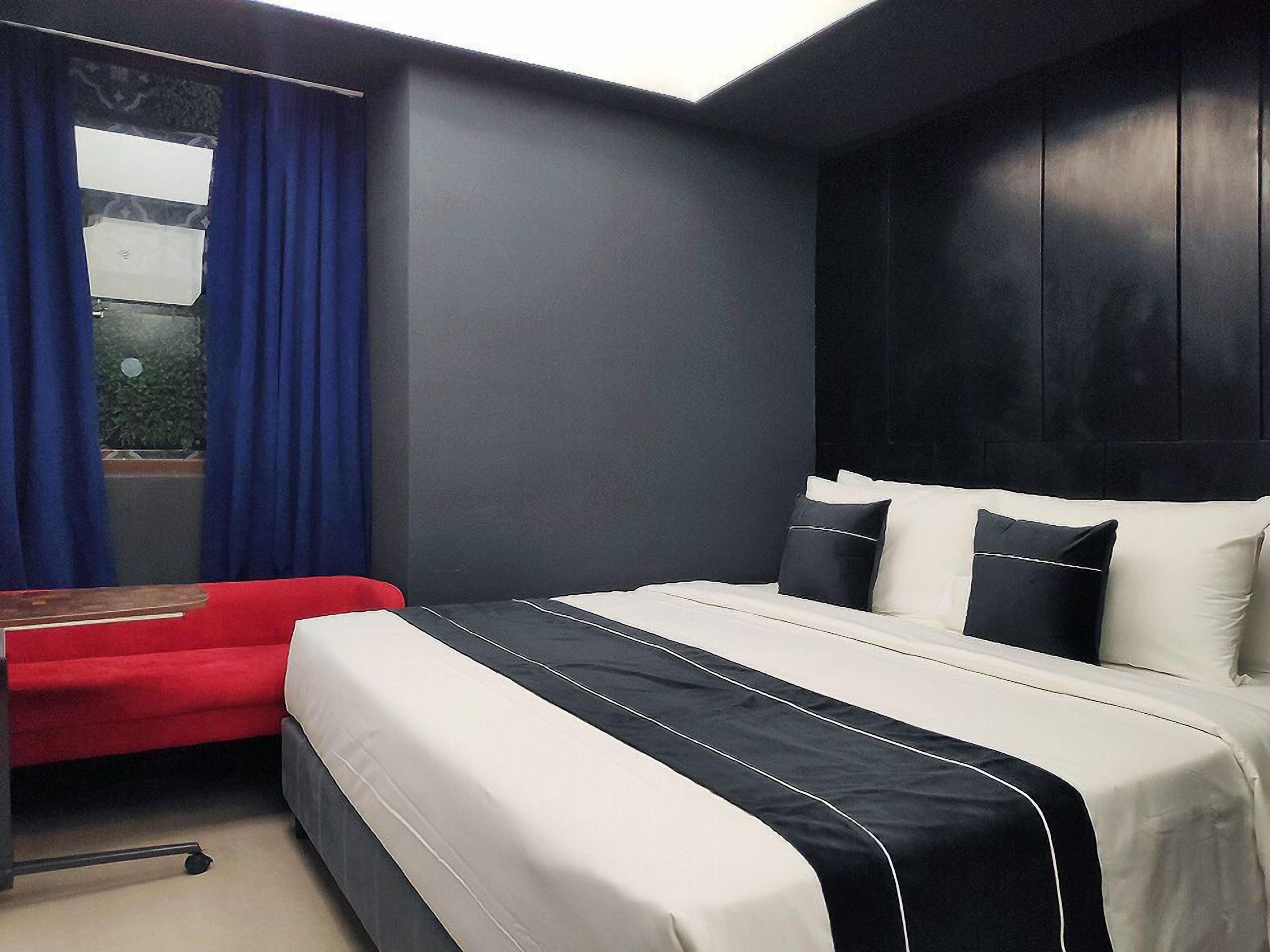 A hotel room with a bed, a desk, and a window with curtains.