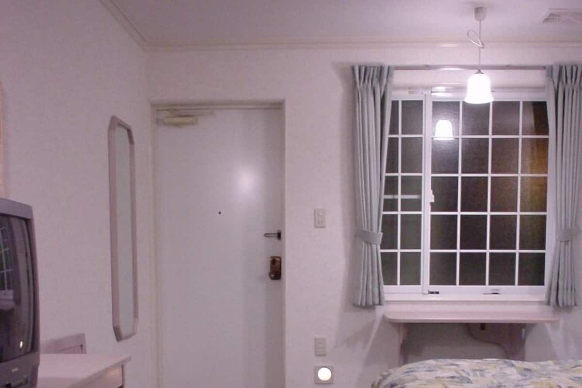 A bedroom with a bed, a desk, a television, and a window with curtains.