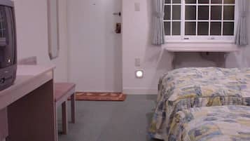 A bedroom with a bed, a desk, a television, and a window with curtains.