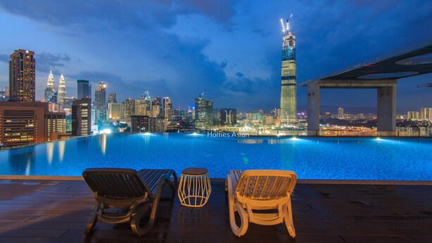 Una piscina en la azotea con sillones de descanso y vistas al horizonte urbano al atardecer.