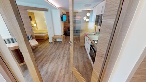 Un interior moderno con suelo de madera, una cama, una mesita, un televisor y una zona de cocina.