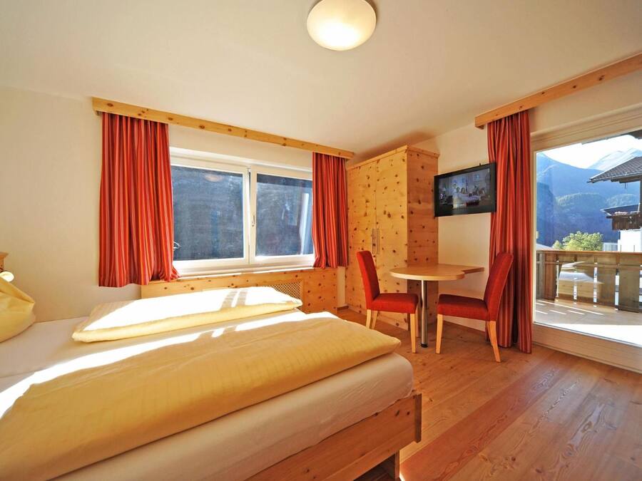Una habitación con cama, una mesa, sillas, televisor y balcón con vista a la montaña.