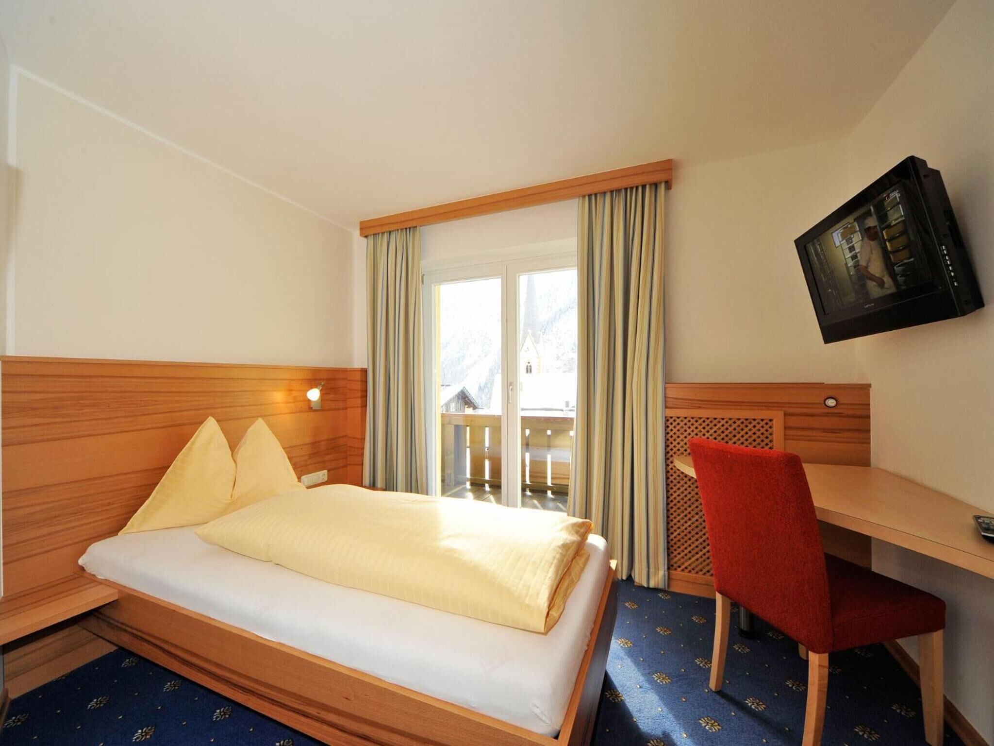 A hotel room with a bed, a desk, a chair, and a TV on the wall.