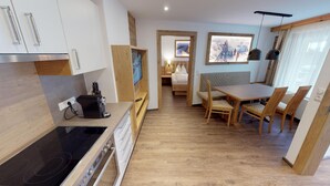 Una cocina moderna con estufa, una zona de comedor con sillas de madera y una cama al fondo.