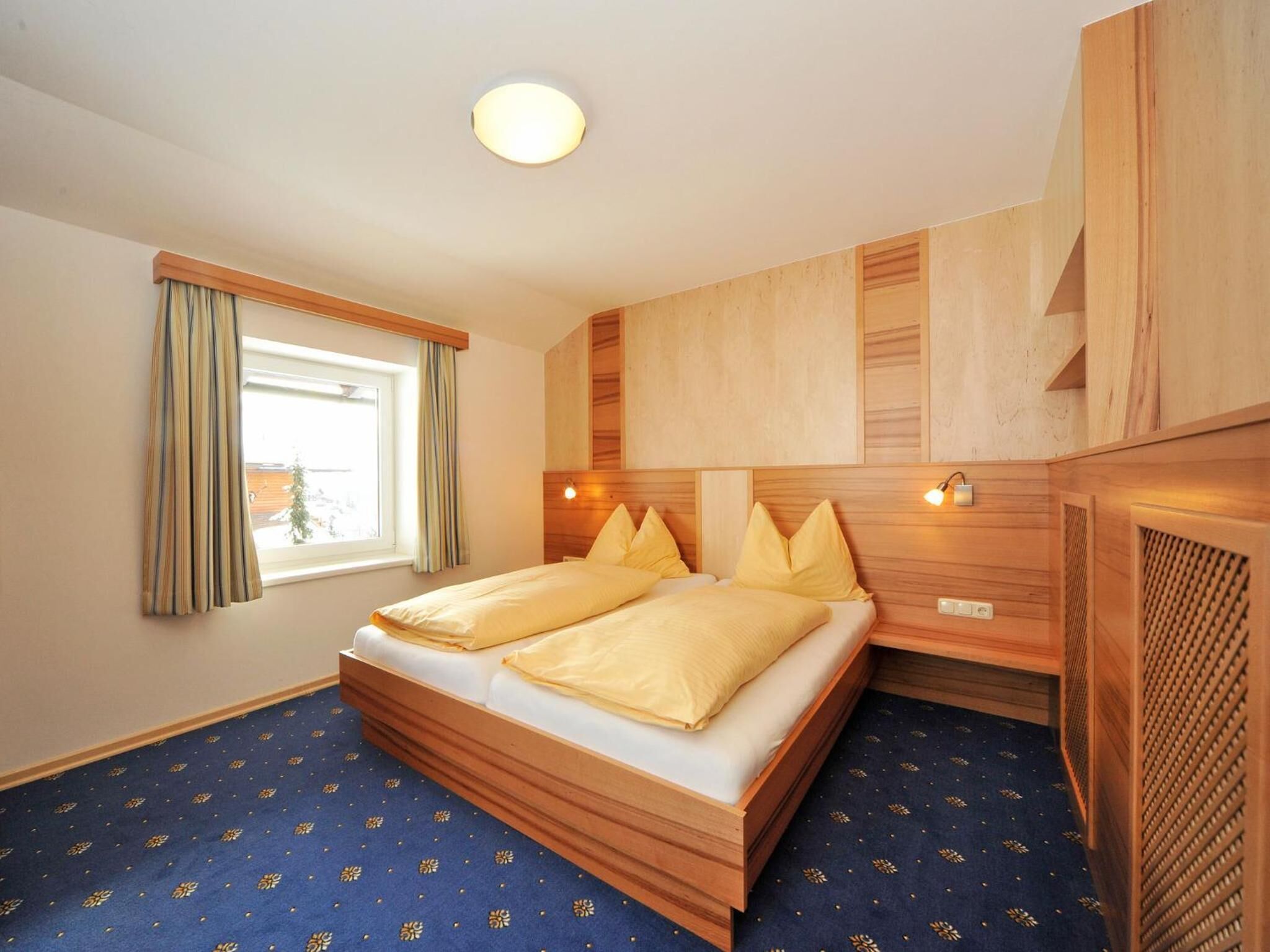 Ein Hotelzimmer mit einem hölzernen Bett, einem fenster mit Vorhängen und einem gemusterten Teppich.