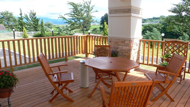 Een houten terras met een tafel en stoelen, omgeven door een witte hek en een stenen pilaar.