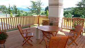 Une terrasse en bois avec une table et des chaises, entourée d’une clôture blanche et d’un pilier en pierre.