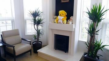 Una sala de estar con un sofá color beige, una chimenea y dos plantas en macetas.