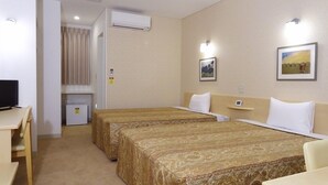 Une chambre d’hôtel avec deux lits, un bureau, une chaise, un petit réfrigérateur, un appareil de climatisation et deux lampes fixées au mur.