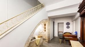 A staircase with a decorative railing, a stone wall, a dining area with a table and chairs, and a wall-mounted light fixture. - Ink Hotel Phos (Rethymno)