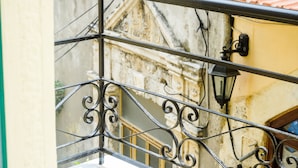 A balcony with wrought iron railings and a view of a building with a tiled roof and a stone wall. - Ink Hotel Phos (Rethymno)