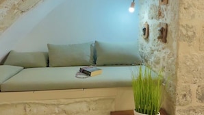 A cozy room with a stone wall, a wooden bench, and a green plant. - Ink Hotel Phos (Rethymno)