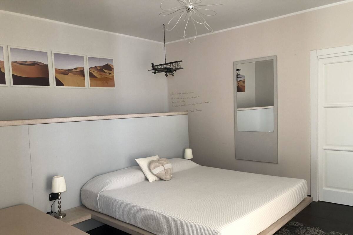 Un dormitorio con cama, una mesita de noche con lámpara, un espejo fijado a la pared y decoración con motivos del desierto.