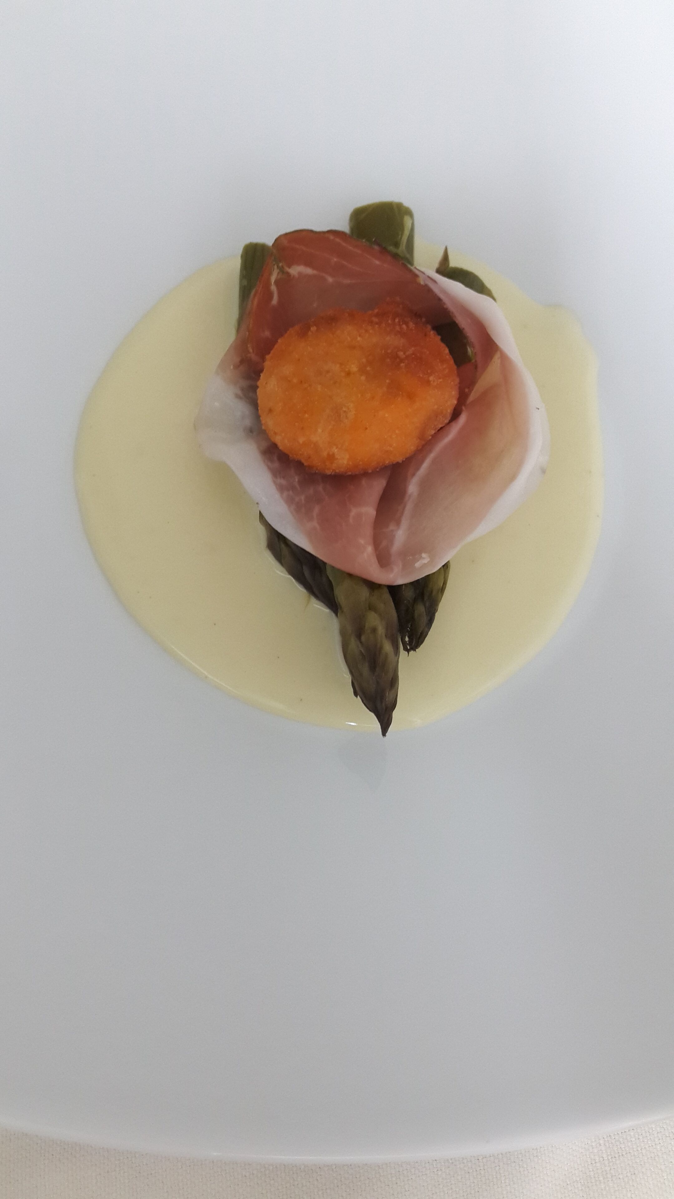 Prato com alimento composto por um pedaço alaranjado, legume verde e molho branco.