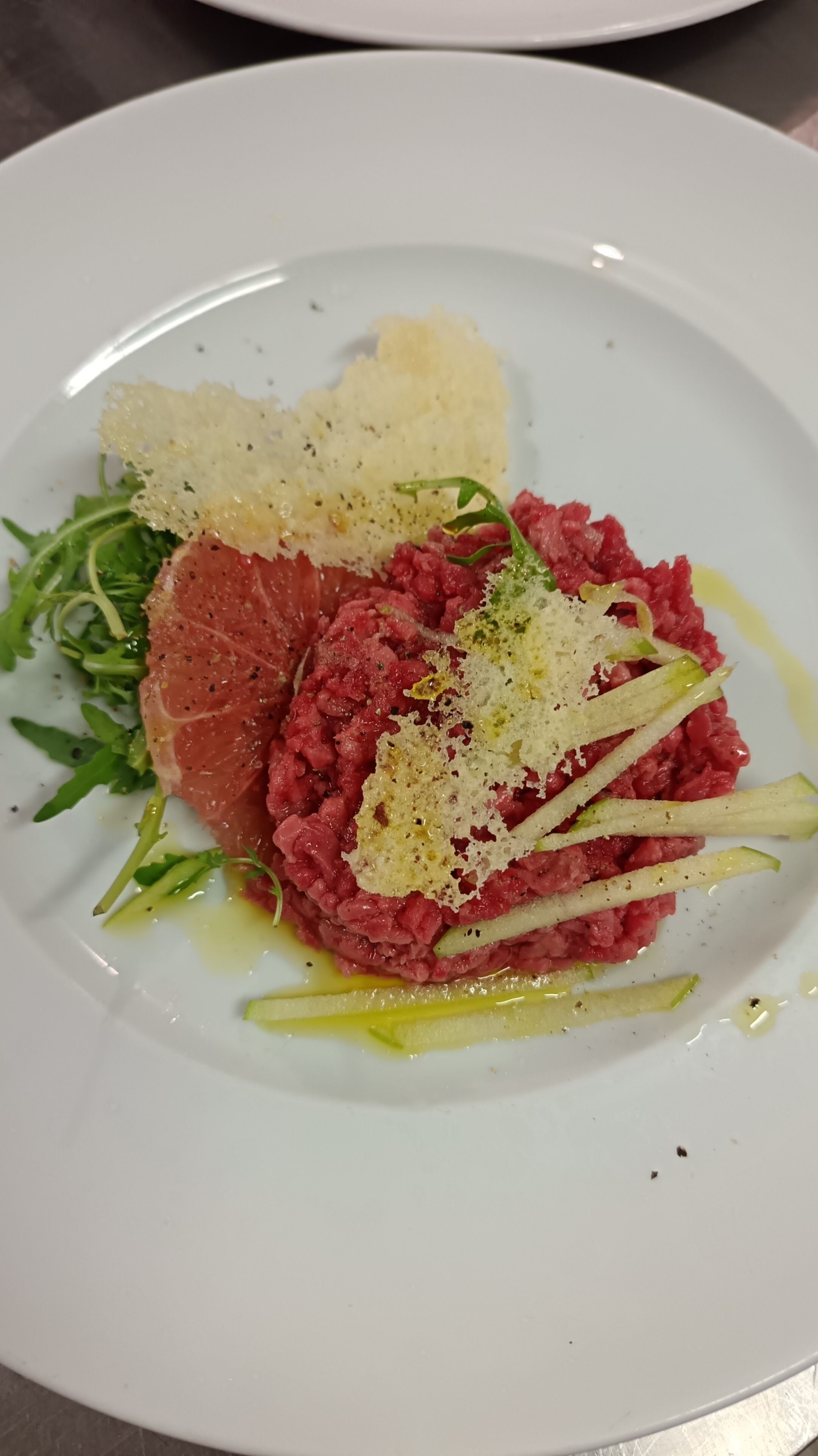 A plate with a dish of raw meat, possibly steak, garnished with herbs and thinly sliced vegetables.