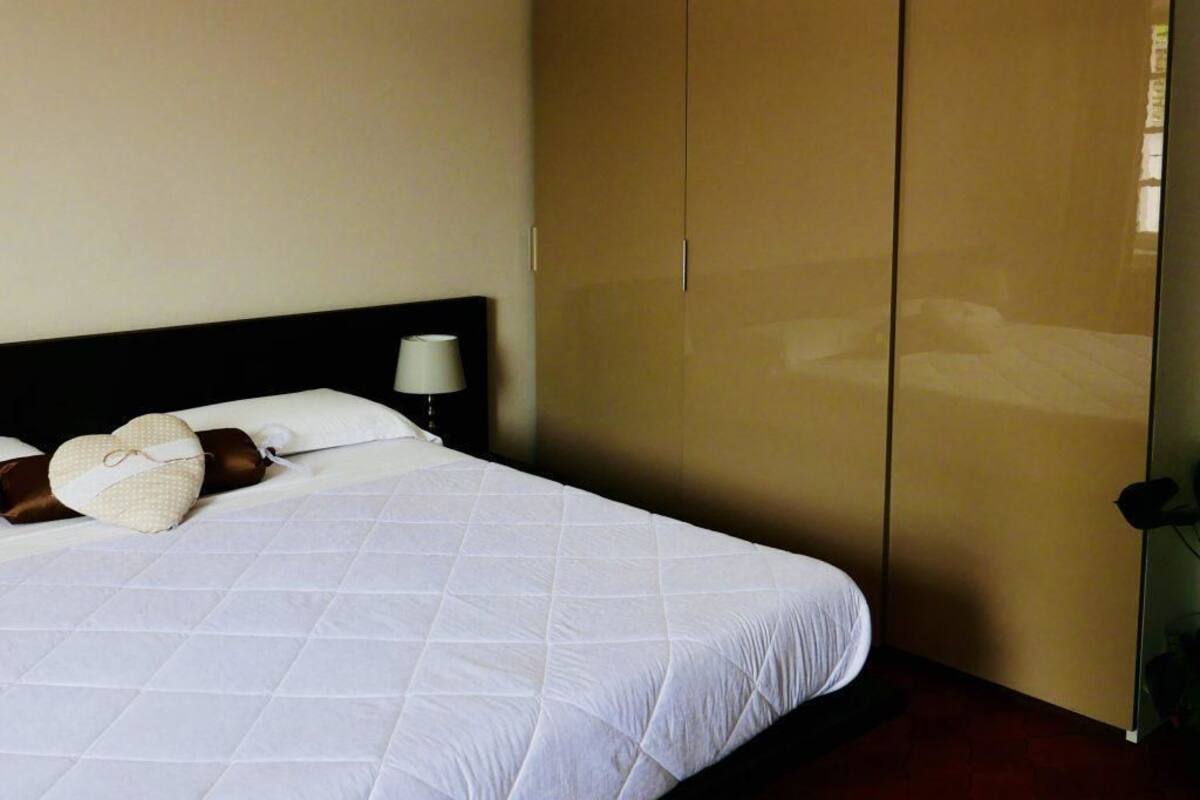 Una habitación de hotel con cama, mesita de noche, lámpara y armario.