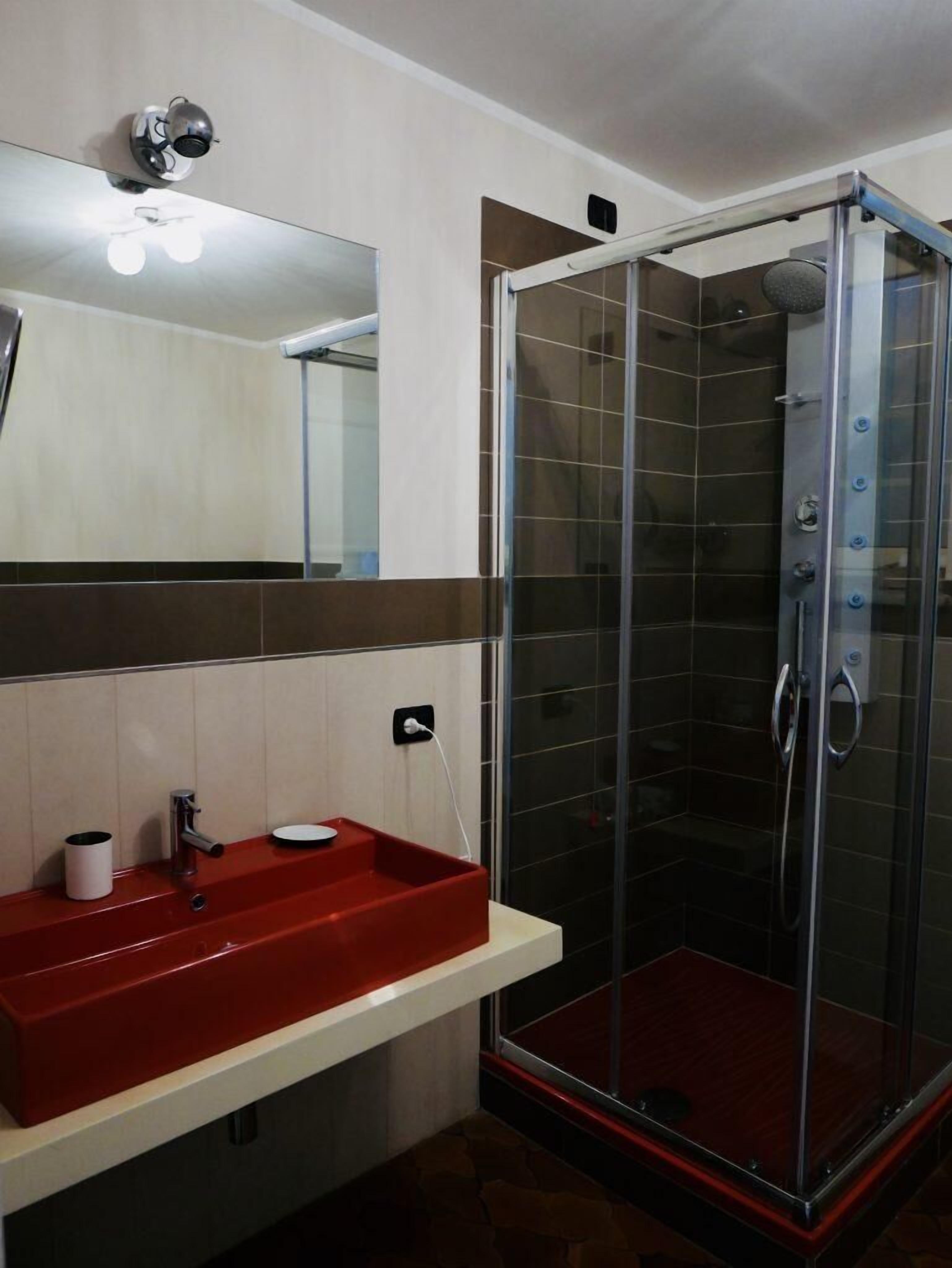 A modern bathroom with a red sink, a glass shower enclosure, and a mirror above the sink.