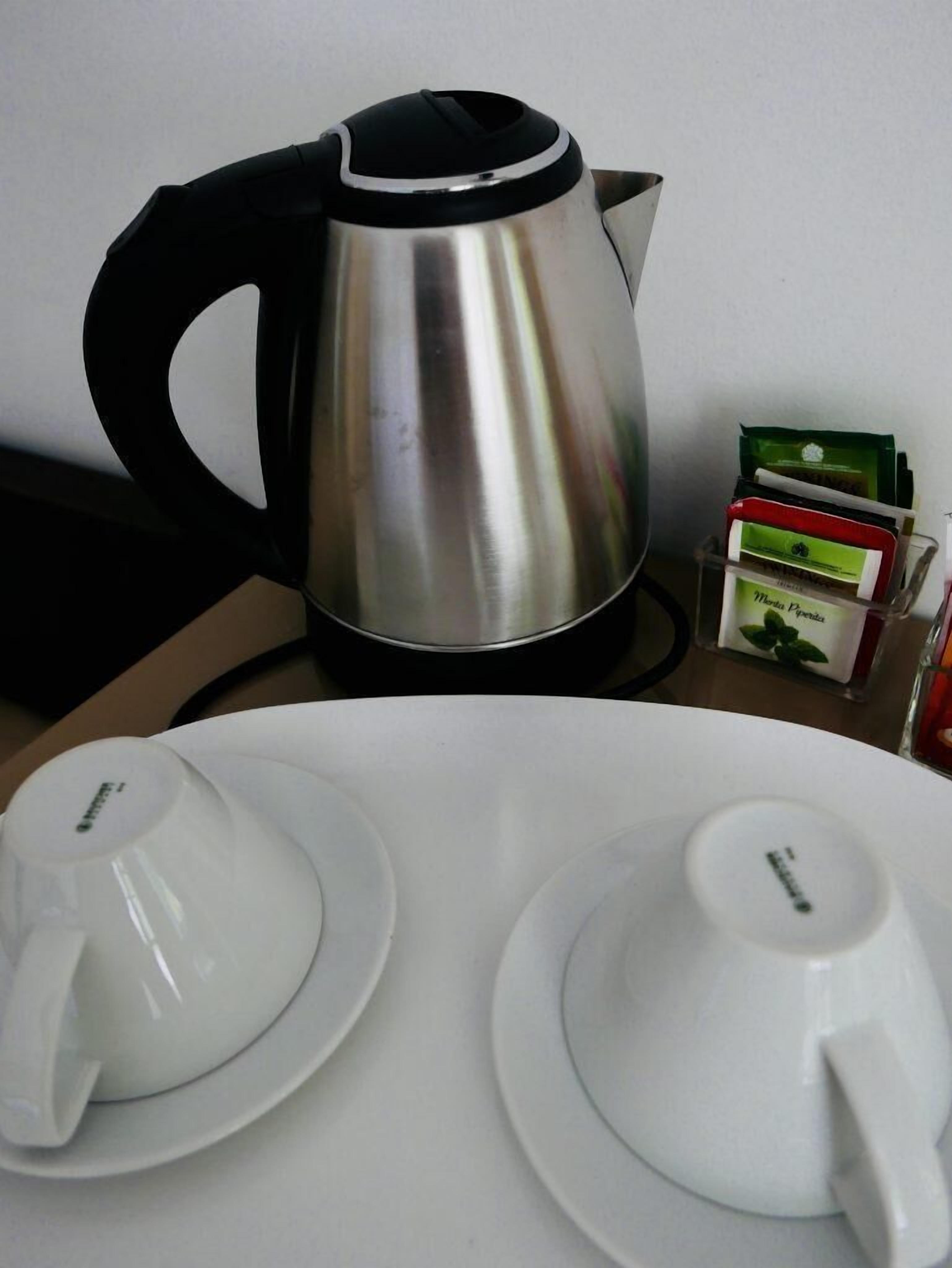 Una tetera de acero inoxidable sobre una mesa con dos tazas y platillos blancos.