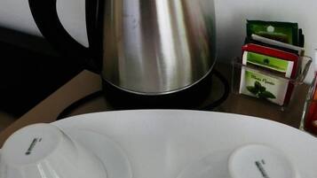 Una tetera de acero inoxidable sobre una mesa con dos tazas y platillos blancos.