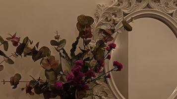 Un jarrón decorativo con flores sobre una mesa, un espejo en la pared y una lámpara de pared.