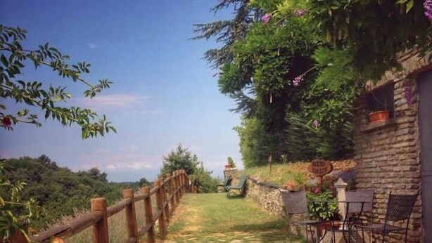 Ein gepflasterter Weg führt zu einer rustikalen Sitzgelegenheit im Freien mit Holzzaun und Steinmauer.