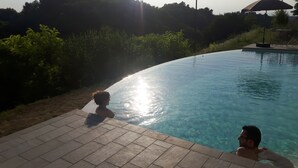Ein Schwimmbecken mit klarem Wasser, umgeben von einer gefliesten Terrasse und üppiger Vegetation.