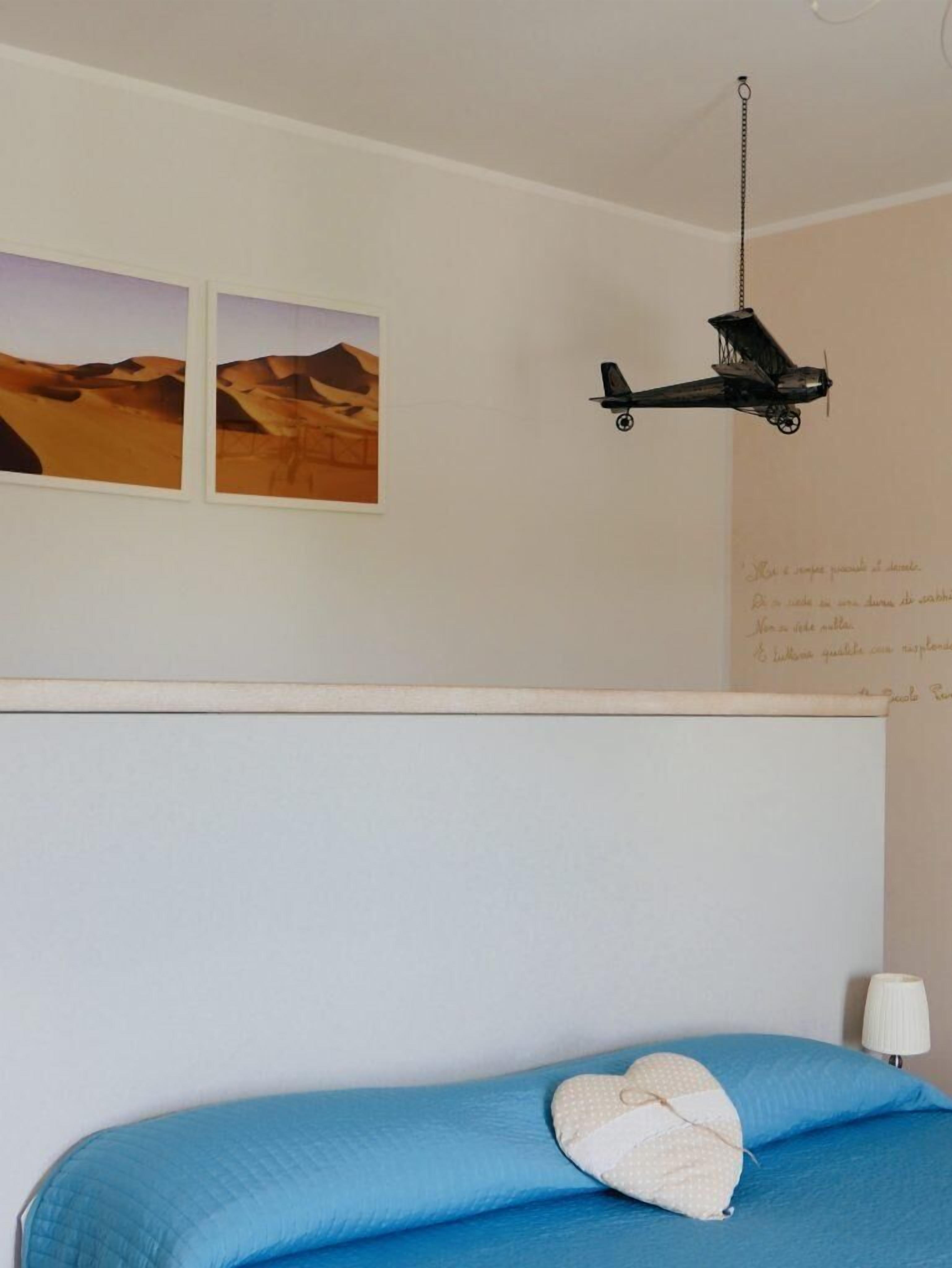 Un dormitorio con una cama, un adorno de avión colgante y dos cuadros de paisajes desérticos en la pared.