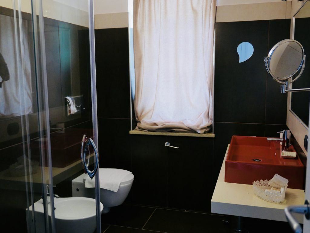 Un baño con cabina de ducha de vidrio, inodoro blanco, lavabo rojo y espejo.