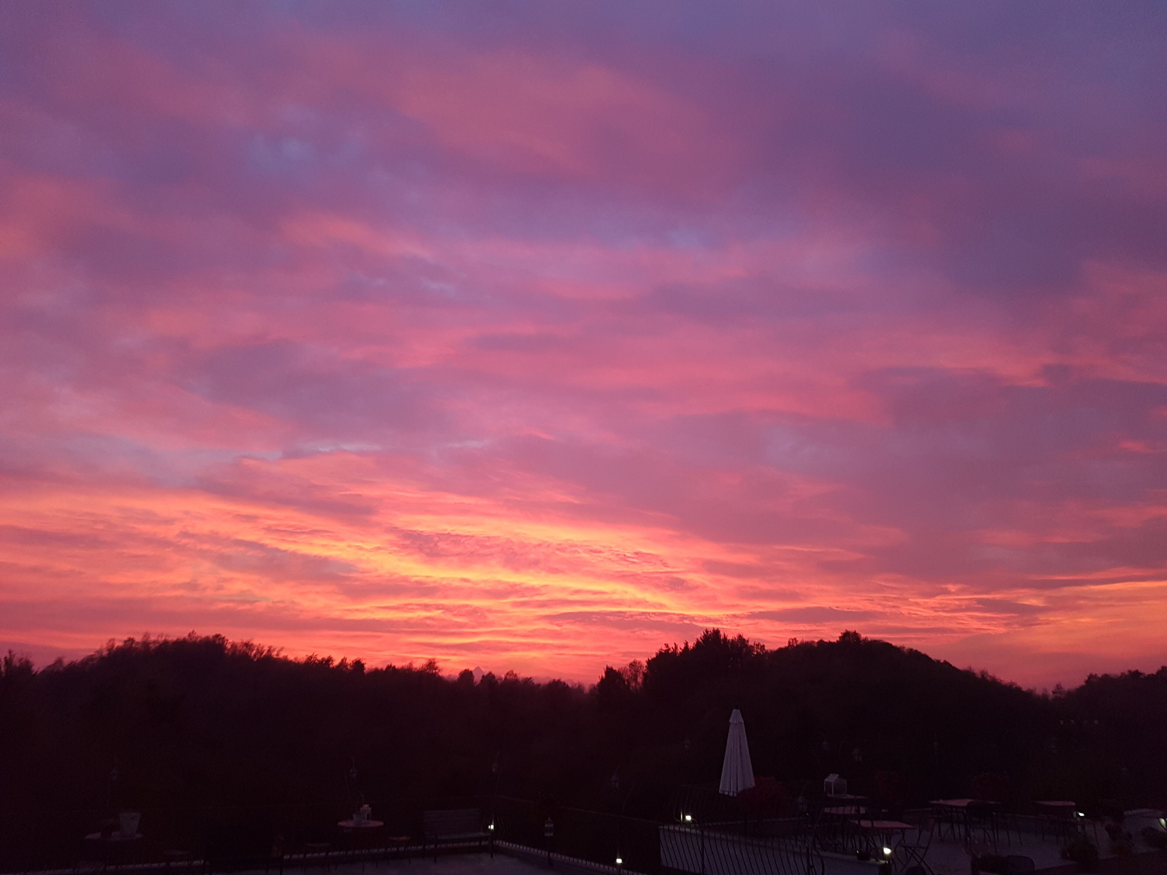 Tramonto su un paesaggio collinare con una statua e una recinzione in primo piano.