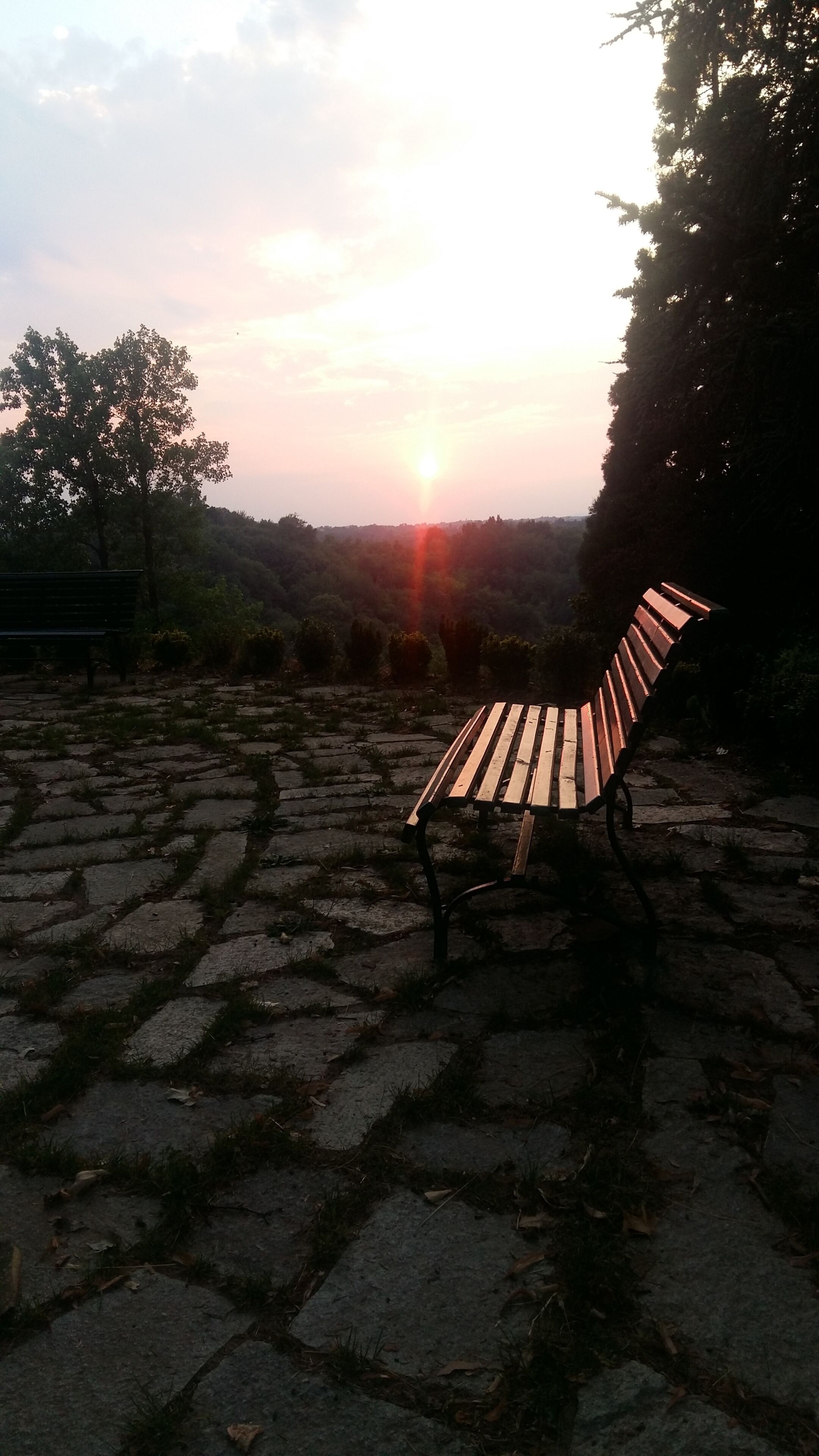 Un banco en una zona empedrada de piedra, con un atardecer de fondo.