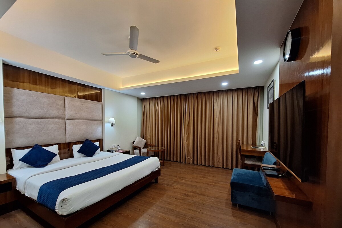 A hotel room with a large bed, a desk, a chair, a ceiling fan, and a TV mounted on the wall.