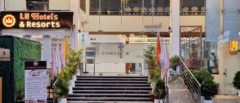 The entrance of LN Hotels & Resorts with a modern design, featuring a staircase leading to the entrance, potted plants, and flags.