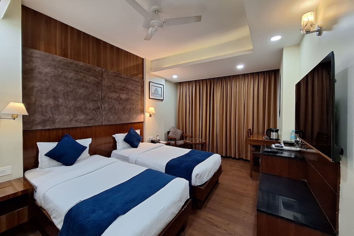 Quarto de hotel com duas camas, um ventilador de teto, televisão, escrivaninha e uma cadeira.