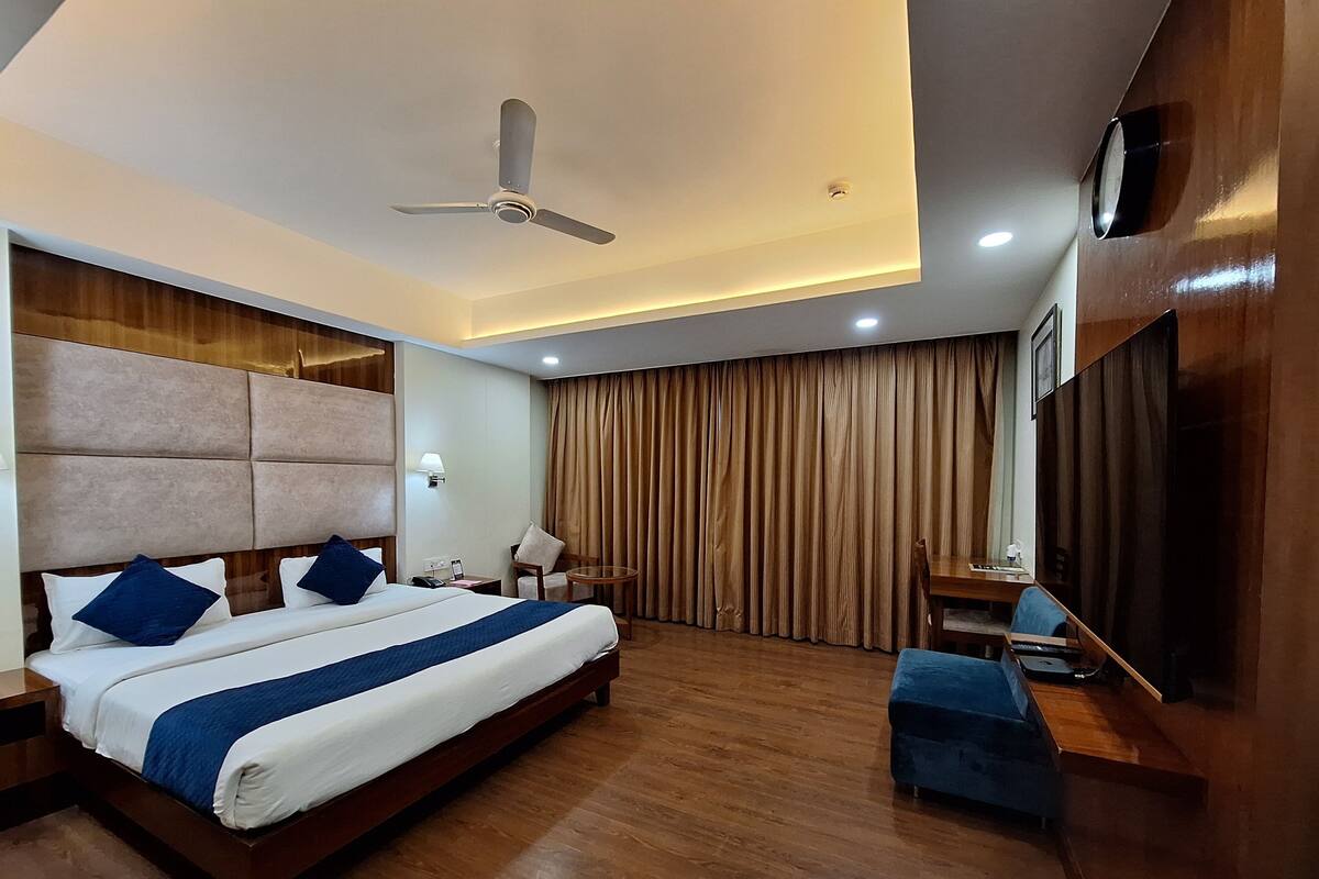 Quarto de hotel com uma cama grande, uma escrivaninha, uma cadeira, um ventilador de teto e uma TV na parede.