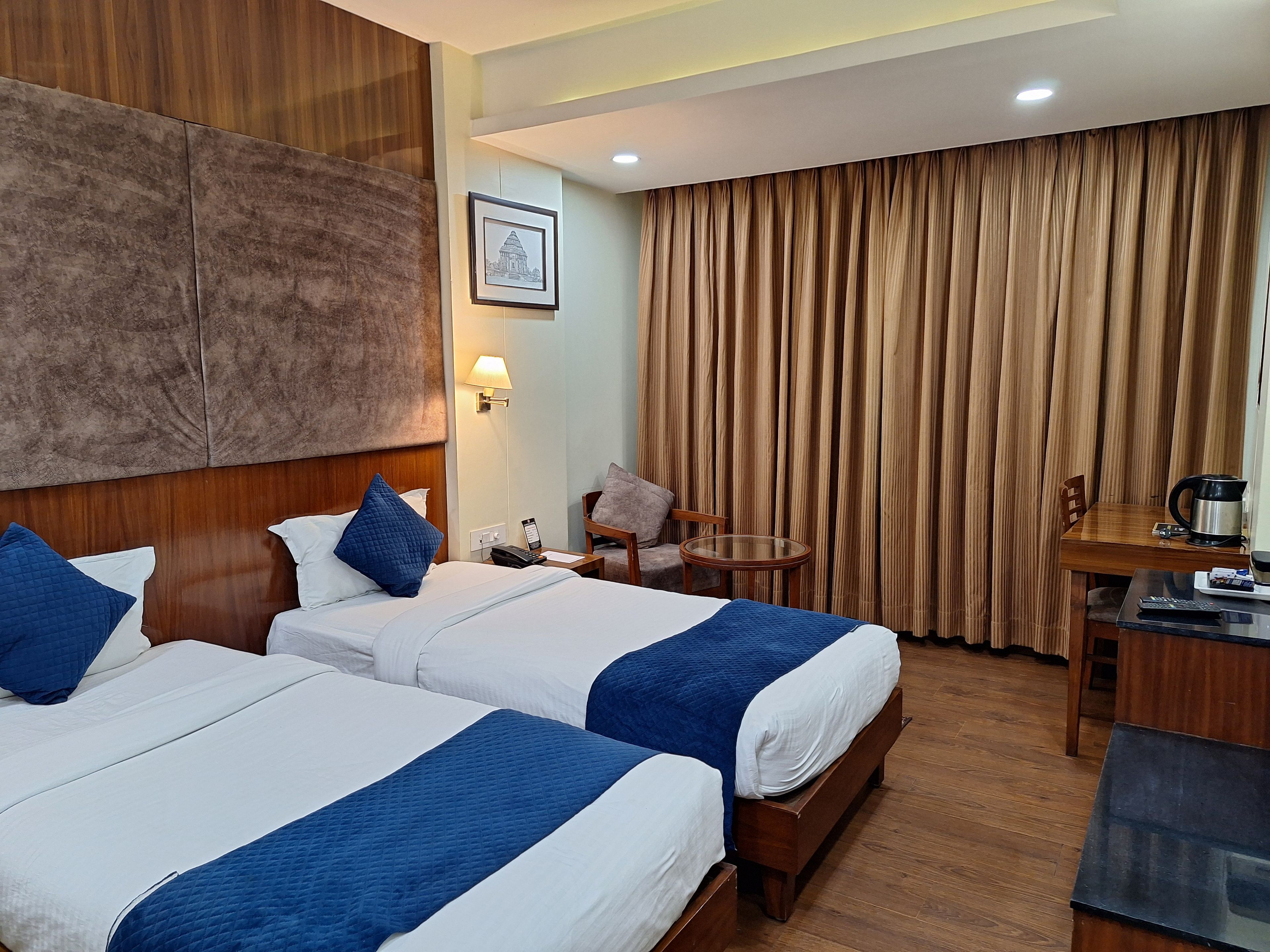 A hotel room with two beds, a desk, a chair, a lamp, and a large window with curtains.