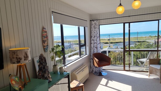 Una habitación con un amplio ventanal que ofrece vistas al mar, un aparador verde, una silla marrón y una pequeña mesa con una lámpara.