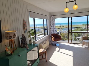 Una habitación con un amplio ventanal que ofrece vistas al mar, un aparador verde, una silla marrón y una pequeña mesa con una lámpara.
