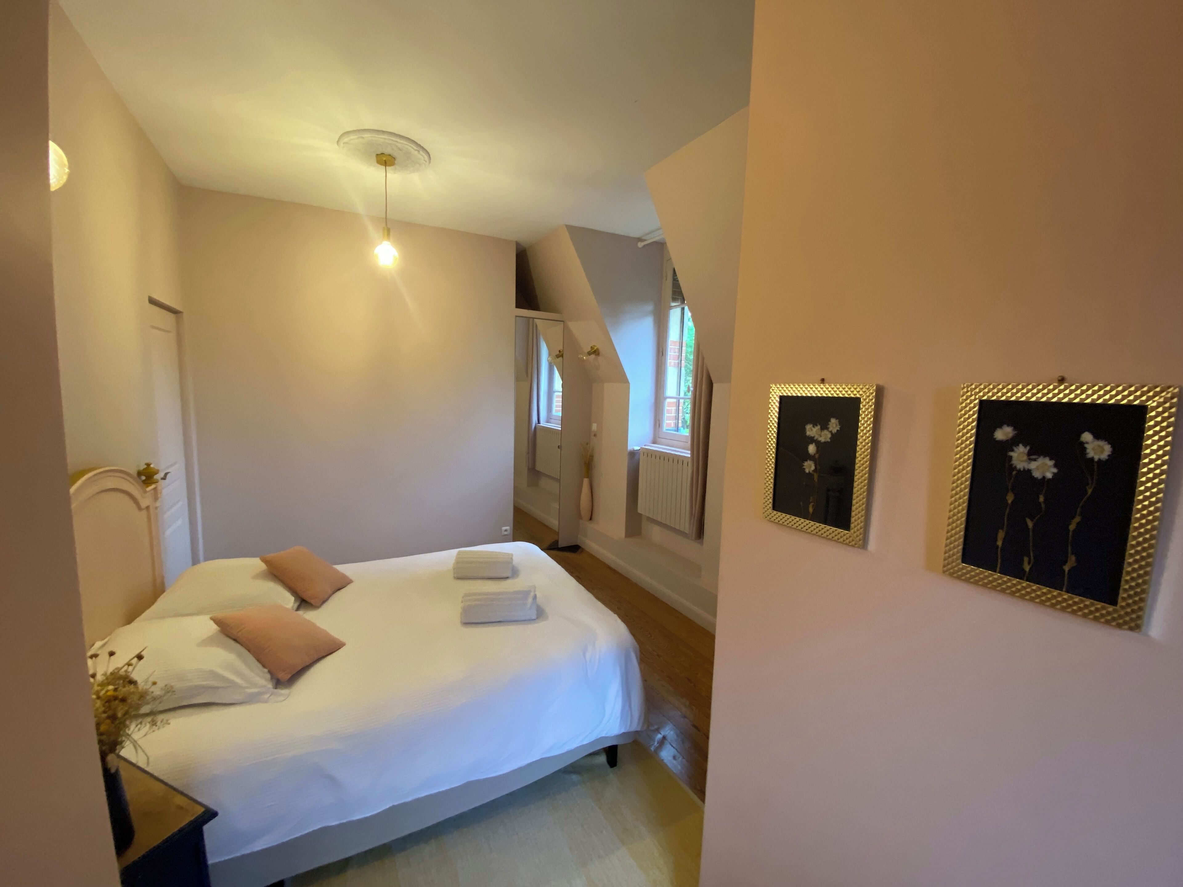 A bedroom with a bed, a nightstand, a window, and two framed pictures on the wall.