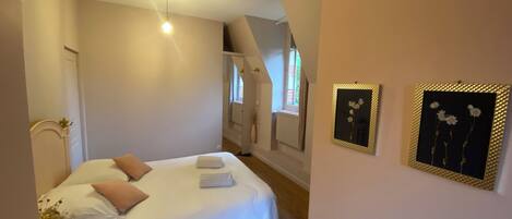 A bedroom with a bed, a nightstand, a window, and two framed pictures on the wall.
