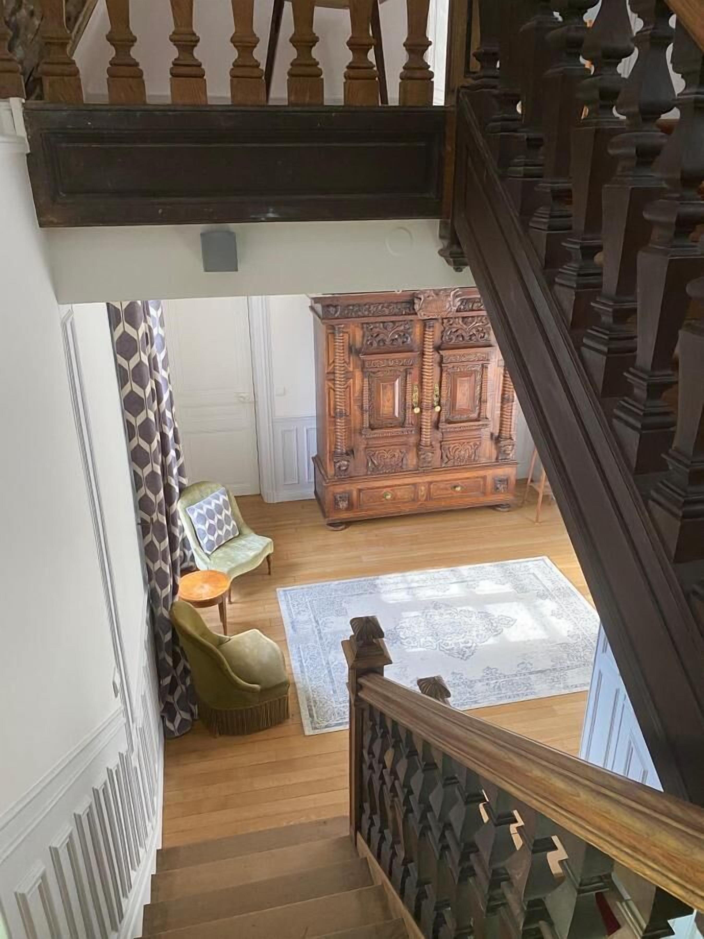 A staircase with a wooden railing leading to a room with a patterned rug, a green armchair, and a wooden cabinet.