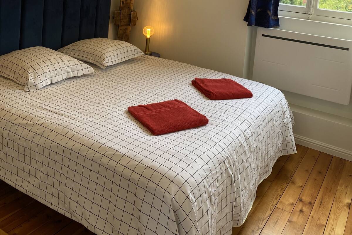Een slaapkamer met een bed, hoofdbord, bedlampen en een raam met gordijnen.