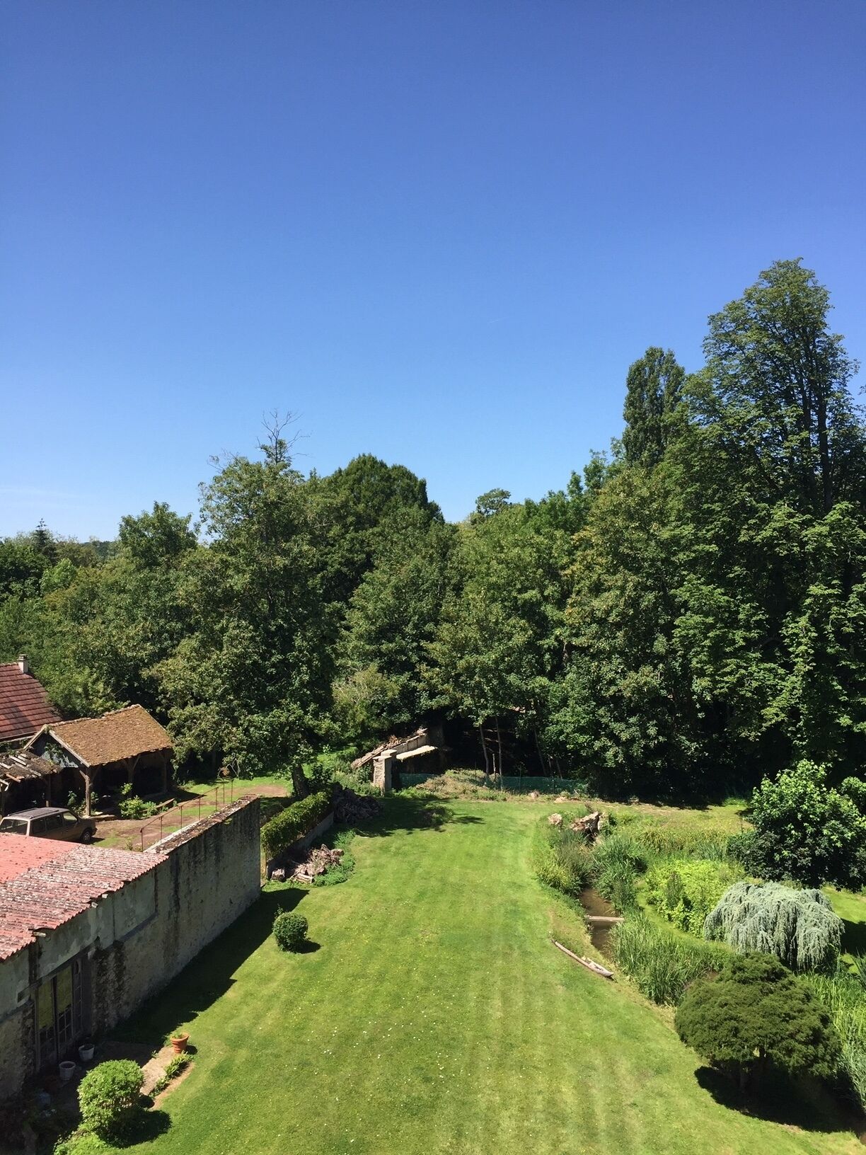 A well-maintained garden with a lawn, a stone wall, and a rustic building with a tiled roof.