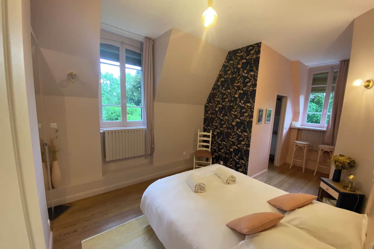 Een slaapkamer met een groot bed, een stoel, een bureau en een raam.